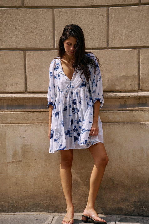 Kyra Mini Dress Deep Sea — full length front view against stone wall, deep sea shibori tie-dye cotton mini dress with V-neckline, balloon sleeves and flared skirt, sandals | Daughters of India