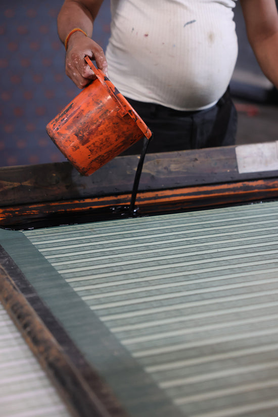 Indian artisan pouring pigment ink onto a screen printing frame during production of Spearmint fabric for Daughters of India, traditional handcraft process