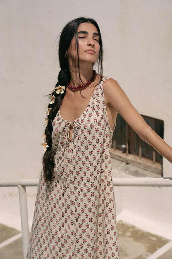 Woman with a braided hair wearing a red beaded necklace and white floral accessories wearing the Daughters of India Sundress Midi in Peony, showing the tie neckline